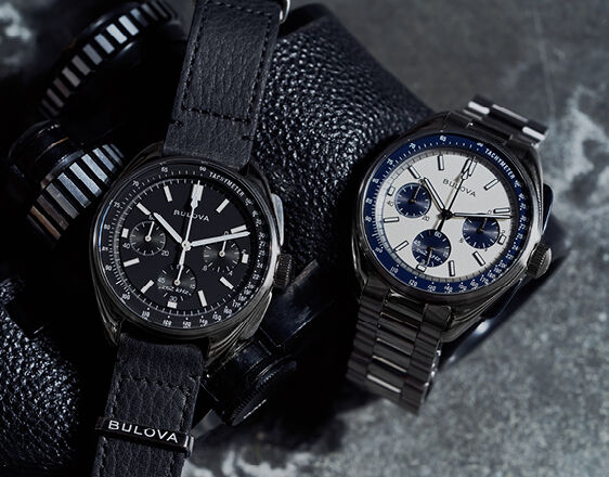 Bulova Archive Series Lunar Pilot chronograph watches – black dial on leather strap and white panda dial on stainless steel bracelet, displayed with binoculars.